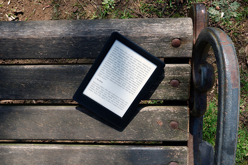 E-book reader standing on an old wooden bench on sunny spring day. Nature and technology concept. Top view and close-up. The text on the screen is a 