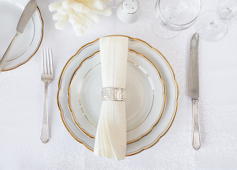 Beautifully decorated table with white plates, glasses, antique cutlery and white coral on luxurious tablecloths