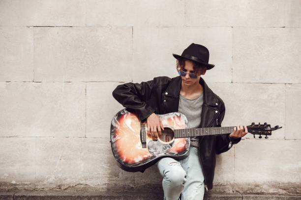 Musician. Guy in hat and sunglasses leaning on wall playing guitar concentrated