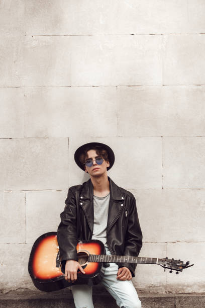 istock Musician. Guy in hat and sunglasses standing isolated on wall with guitar posing cool 1208307825