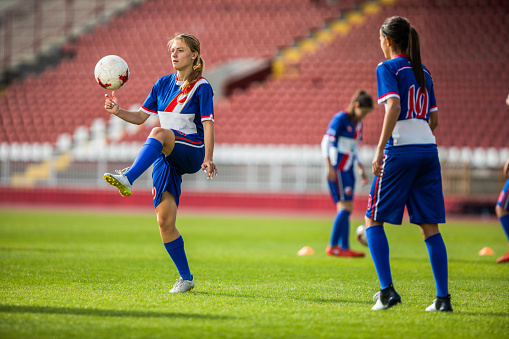 Female soccer players warming up before the soccer match on a playing field. Focus is on girl with a ball.