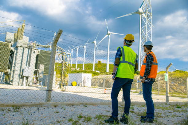 giovani lavoratori che guardano e controllano le turbine eoliche sul campo - stazione sussidiaria elettrica foto e immagini stock