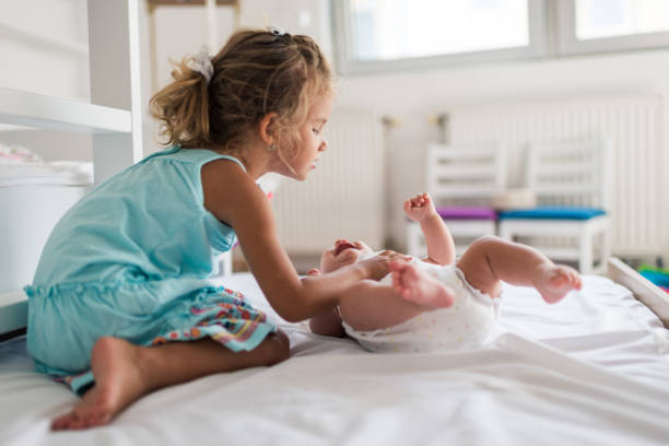 Child watching newborn baby in bassinet. Sibling meeting new family member. Kids play in white bedroom. Nursery crib bedding and textile for young kid. Siblings love.