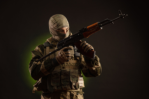 soldado milicia saboteador en ropa militar con un rifle Kalashnikov en un fondo oscuro photo
