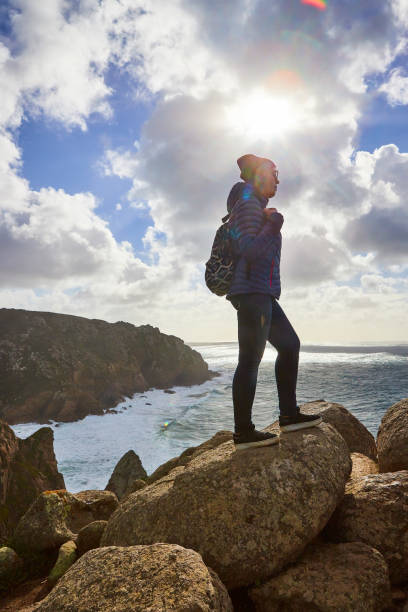 young woman tourist at cape cabo da roca standing on the rocky edge of the cliff. the waves of the ocean break on the rocks at the bottom of the cliff - hiking coastline waters edge sunny imagens e fotografias de stock
