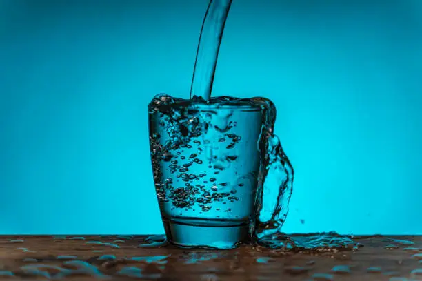 Photo of Pouring glass of water - blue background, overflowing