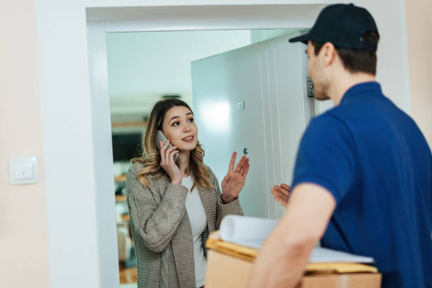 istock Young woman talking on mobile phone while receiving home delivery form a courier. 1208317975