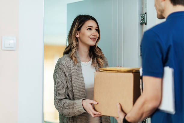 Smiling woman receiving a package from delivery man at home. Young woman standing on a doorway while receiving package form a courier. delivery person stock pictures, royalty-free photos & images