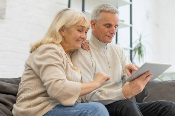 istock Happy elderly couple using gadget in living room 1208318810