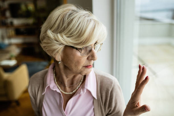 istock Thoughtful senior woman touching the window while looking through it. 1208320684