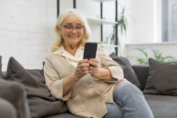 istock Happy elderly woman using smartphone in living room 1208320797