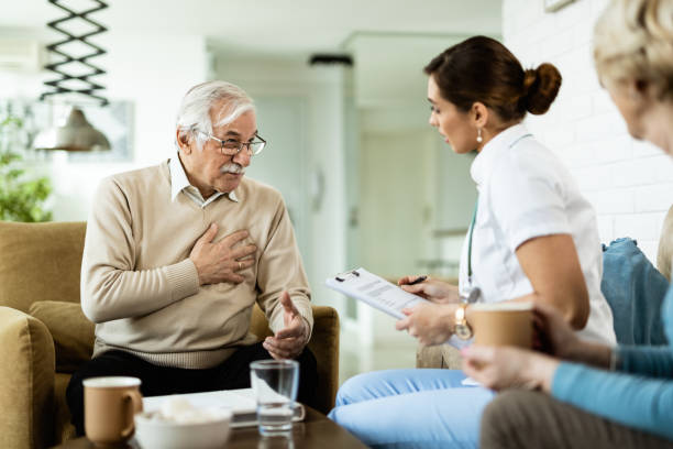 starszy mężczyzna narzeka na ból w klatce piersiowej podczas rozmowy z lekarzem w domu. - nurse illness doctor heart disease zdjęcia i obrazy z banku zdjęć
