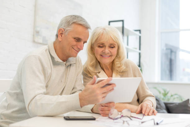 istock Smiling older couple holding gadget at home 1208323656