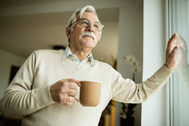 istock Pensive mature man with cup of coffee looking through the window. 1208323864