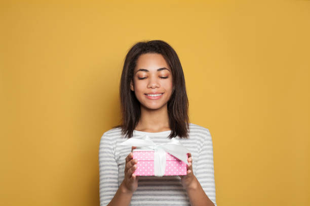 istock Happy black woman with gift having fun on bright yellow background 1208325139