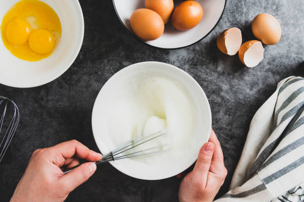 Whipping white eggs with whisk, in a palte. Top view of woman's hands mixing eggs, cooking pastry. Whipping white eggs with whisk, in a palte. Top view of woman's hands mixing eggs. whipped food stock pictures, royalty-free photos & images
