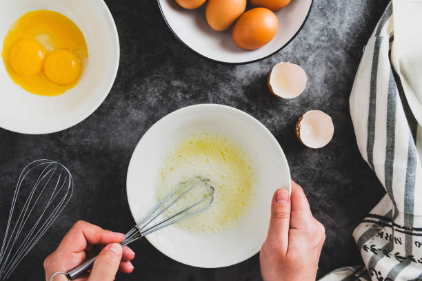 istock Cooking omlette. Woman's hands cookingomlette, breaking an fresh egg. Dark background. Food flat lay. 1208326632