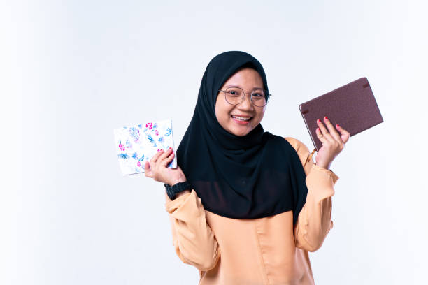 右手と左手で本を持っている笑顔のかわいいアジアの女の子.白い背景の上に隔離されたカメラを見て - looking at camera smiling desk isolated ストックフォトと画像