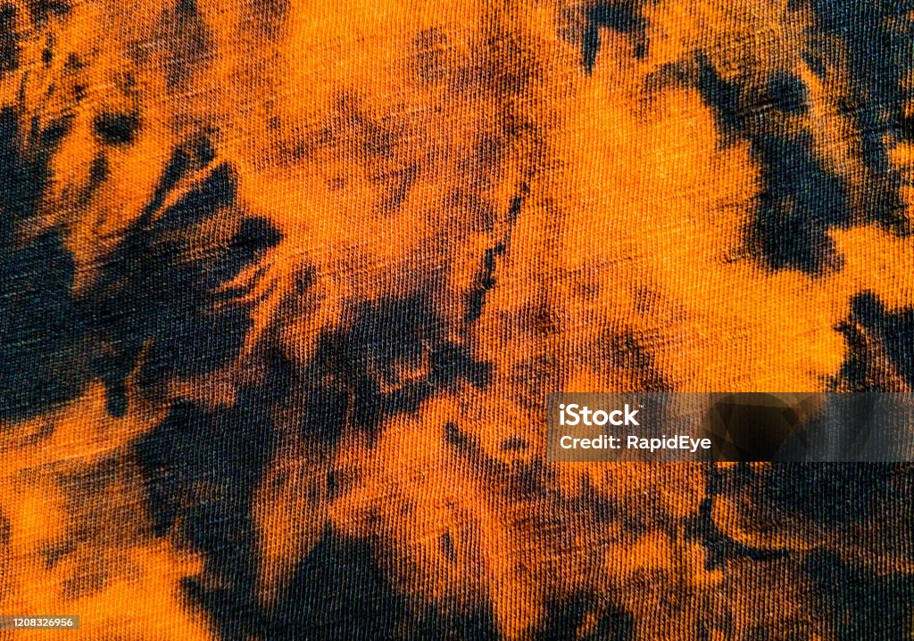 Macro shot of tie-dyed textile as background An extreme close-up of fabric tie-dyed in orange and black for use as background. Tie Dye Stock Photo