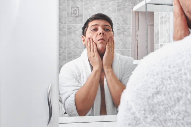 istock a man in a white bathrobe looks in the mirror in the bathroom. 1208328497