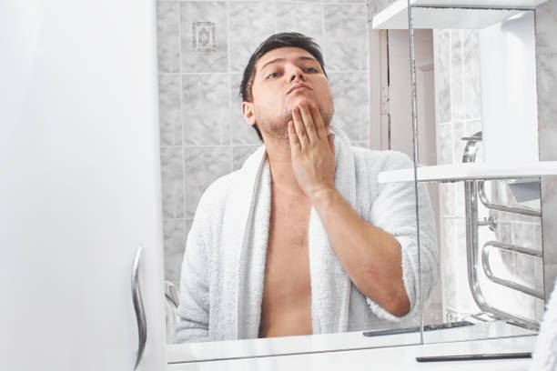 istock a man in a white bathrobe looks in the mirror in the bathroom. 1208328518