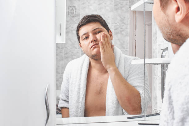 istock a man in a white bathrobe washes his face with soap through a bathroom mirror. 1208328534