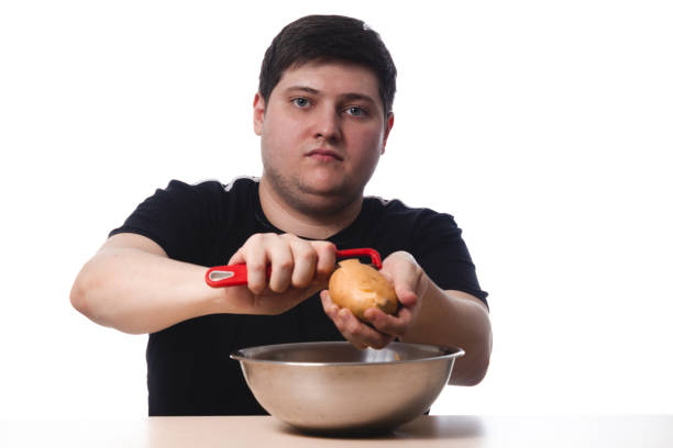 A young guy in a black T-shirt peels potatoes. on white background. isolate. copy space