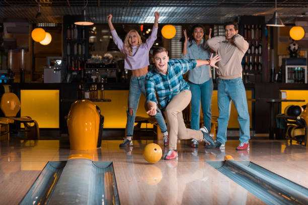istock handsome young man throwing bowling ball near excited multicultural friends 1208329987