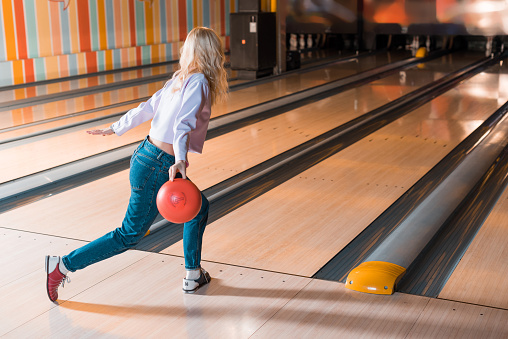 young blonde woman throwing bowling ball on skittle alley