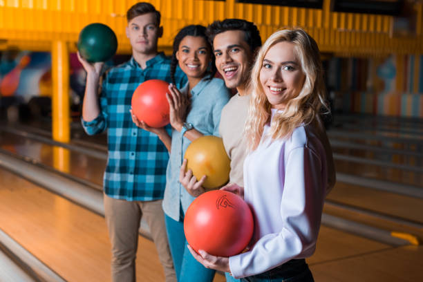 istock happy multicultural friends holding bowling balls and looking at camera while standing in bowling club 1208330003