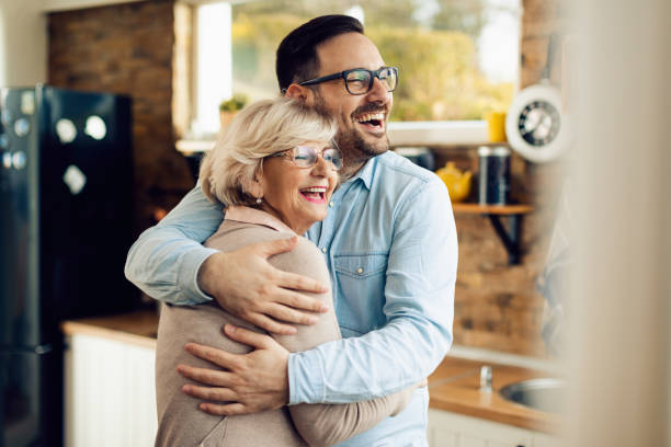 Cheerful man and his mature mother embracing in the kitchen. Cheerful senior woman embracing her mid adult son who came to visit her at home. son stock pictures, royalty-free photos & images