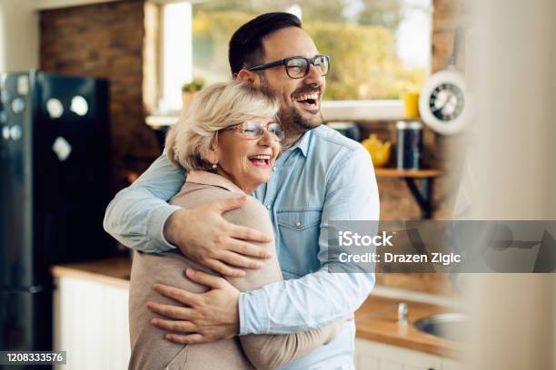 Cheerful Man And His Mature Mother Embracing In The Kitchen Stock Photo - Download Image Now