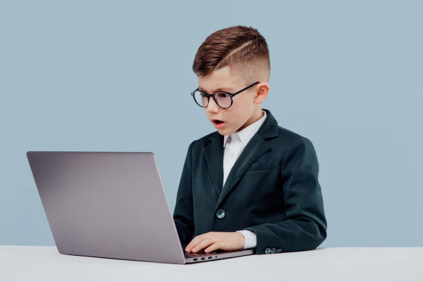 istock stressed little child boy in suit and glasses  reading data from laptop while working on  project against blue background 1208334420