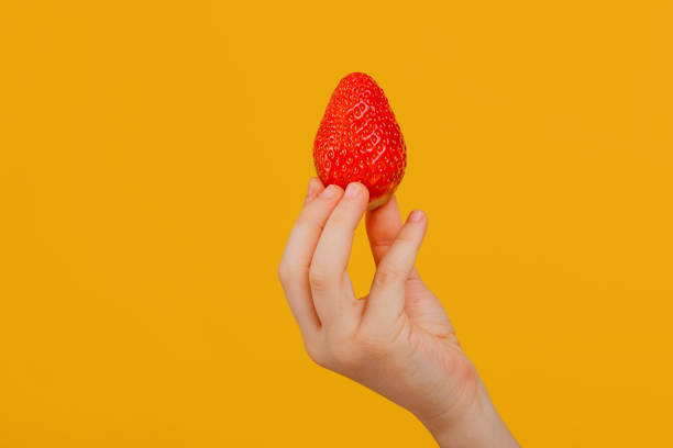 istock child's hand with strawberry, isolated on yellow background 1208334490