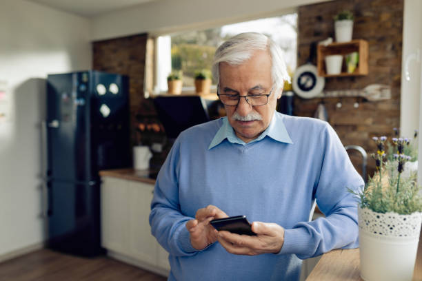 Senior man text messaging on mobile phone in the kitchen.