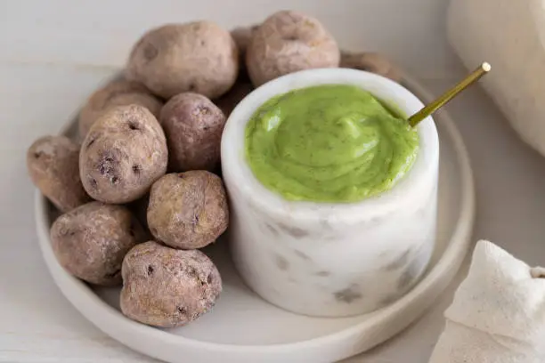 Photo of Mojo verde or Green sauce with with Papas Arrugadas or wrinkly potatoes with salt on wooden table .Close up