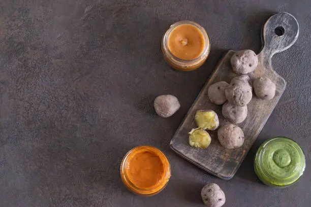 Photo of Canary Islands popular dish Papas Arrugadas, wrinkly potatoes with Mojo picon ,Red hot sauce, and  Mojo verde , Green sauce and Almogrote, chesse sauce on concrete background. Top view