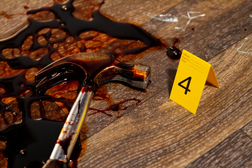 Forensic markers and bloodied weapons in a simulated murder/homicide crime scene with broken glass. Hard flash illumination adds to genuine atmosphere.