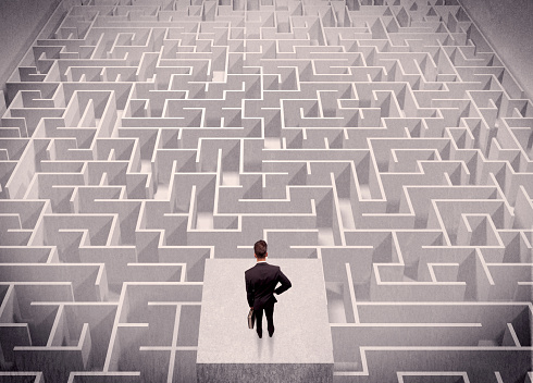 A confused businessman thinking while standing on a square platform above a detailed maze