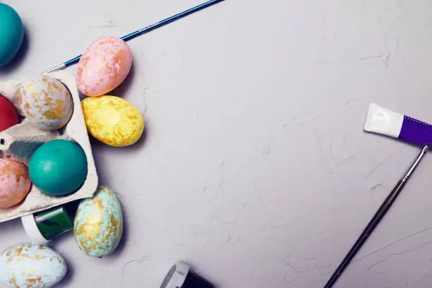 Happy easter. Colored eggs on gray concrete. Flowering, fur-seal willow, on an abstract gray background. Multicolored paints, brushes, watercolor. Space for text, empty space, flat lay.