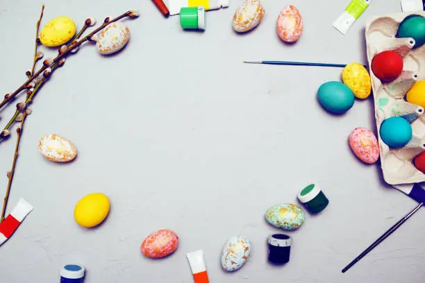 Happy easter. Colored eggs on gray concrete. Flowering, fur-seal willow, on an abstract gray background. Multicolored paints, brushes, watercolor. Space for text, empty space, flat lay.