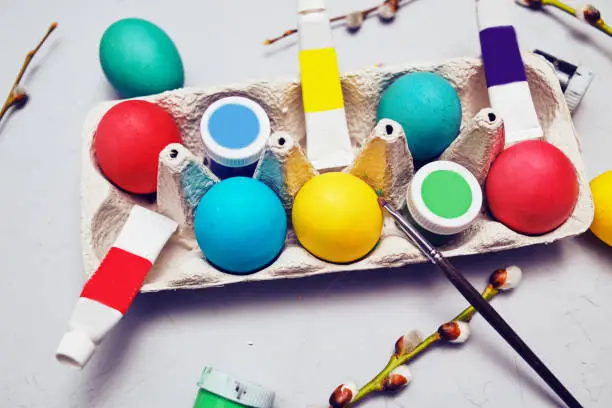 Happy easter. Colored eggs on gray concrete. Flowering, fur-seal willow, on an abstract gray background. Multicolored paints, brushes, watercolor. Real eggs and paint