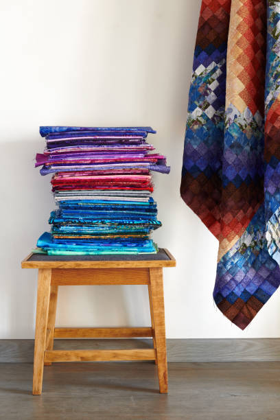 istock Stack of fabrics on a stool and quilt top made in the bargello style on neutral wall background 1208341358