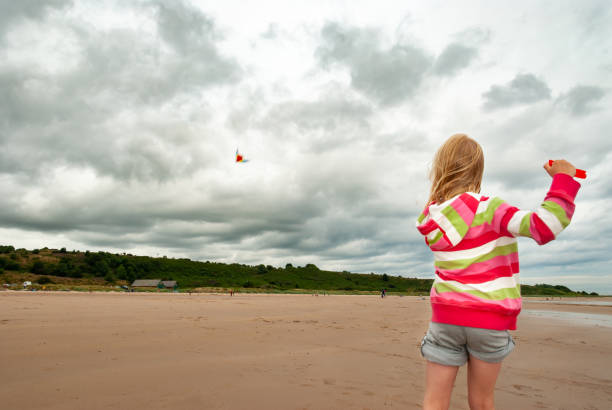 istock Young girl flying kite on beach with dramatic clouds in the background 1208341566