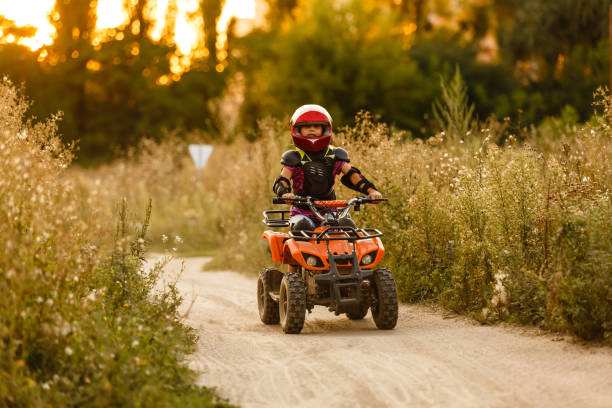 the little girl rides a quad bike atv. a mini quad bike is a cool girl in a helmet and protective clothing. electric quad bike electric car for children popularizes green technology. - helmet bicycle little girls child imagens e fotografias de stock