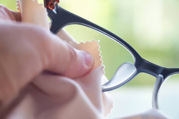 istock Woman's left hand cleaning grey shortsighted or nearsighted eyeglasses by beige microfibre cleaning cloths, Bokeh green background, Close up & Macro shot, Selective focus, Optical concept 1208344222
