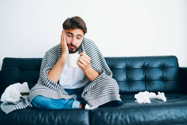 istock Young man sitting on couch while stating at home sick with the flu virus 1208345063