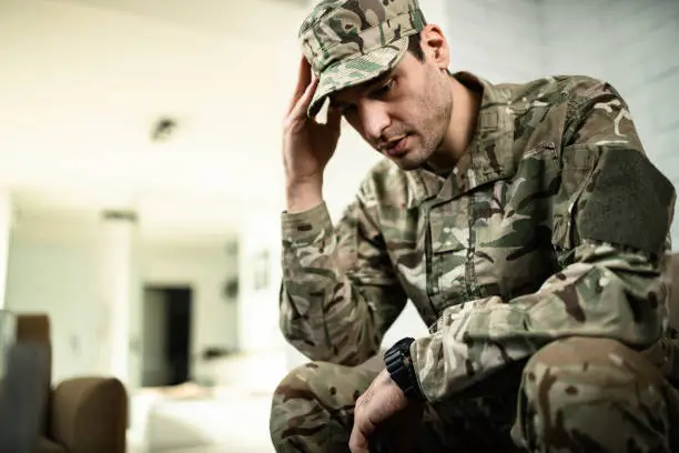 Young pensive military officer feeling sad while sitting alone at home.