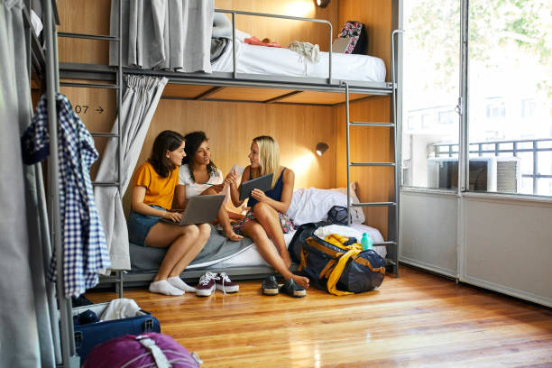 Friends planning trip on bunkbed in dorm room Female friends discussing while sitting on bunkbed. Young women are using technologies and talking over map. They are planning trip at dorm room in hostel. dorm room photos stock pictures, royalty-free photos & images