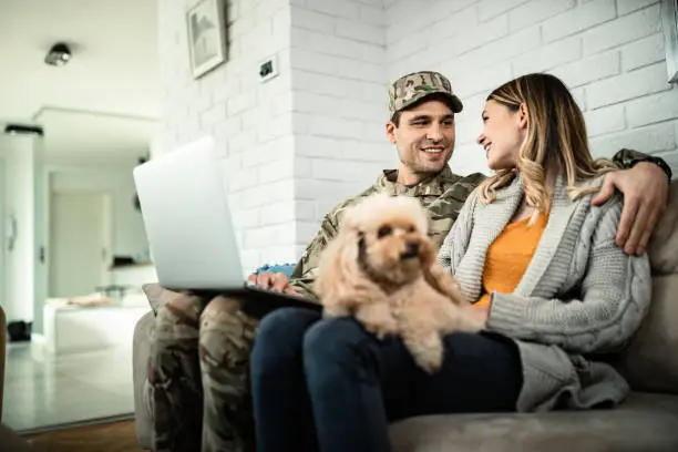 Photo of Happy military couple communicating while using laptop at home.